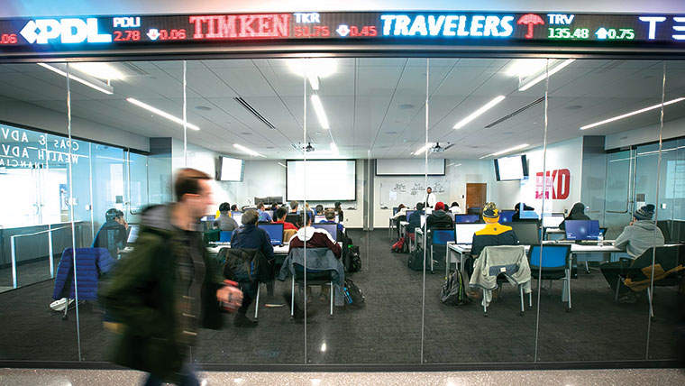 Student walking past a business class with stock market ticker on display
